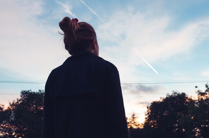 The silhouette of a young woman looking at sunset in the distance.